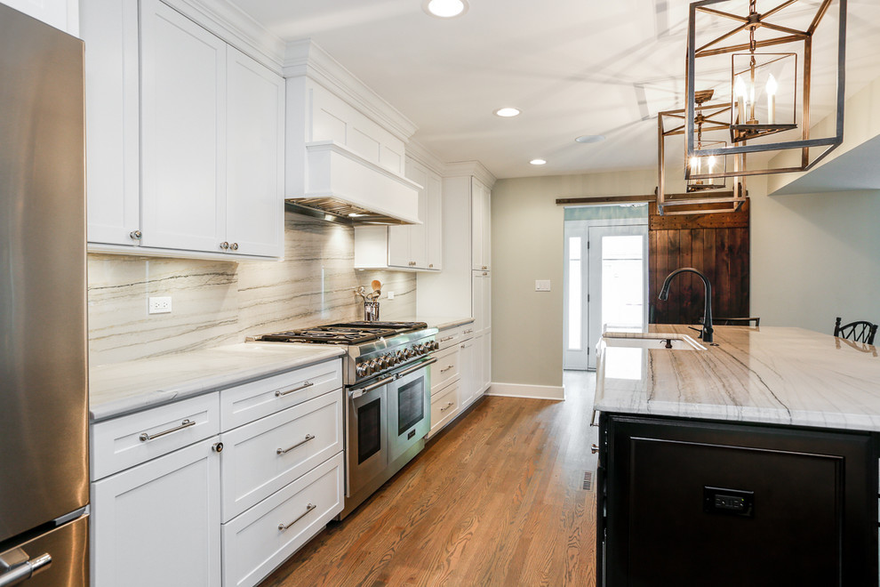 Example of a large cottage galley medium tone wood floor open concept kitchen design in Chicago with a farmhouse sink, shaker cabinets, white cabinets, marble countertops, gray backsplash, stone slab backsplash, stainless steel appliances and an island