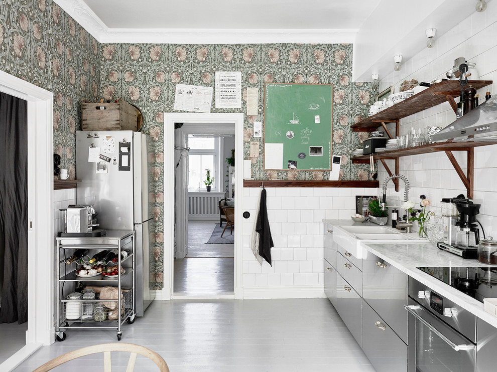 Mid-sized scandinavian single-wall kitchen in Gothenburg with a farmhouse sink, white splashback, stainless steel appliances, painted wood floors, flat-panel cabinets, stainless steel cabinets, marble benchtops and no island.