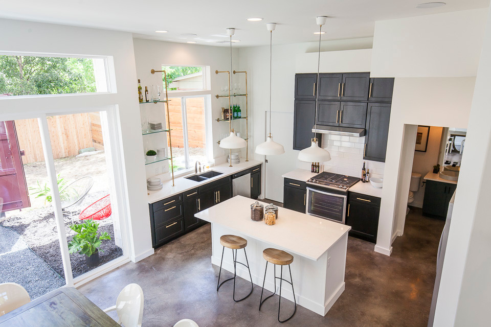 Large contemporary eat-in kitchen in Austin with a double-bowl sink, shaker cabinets, black cabinets, quartz benchtops, white splashback, subway tile splashback, stainless steel appliances, concrete floors and with island.