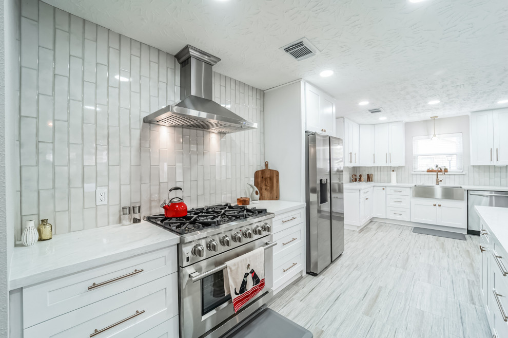 Large classic l-shaped kitchen/diner in Houston with a belfast sink, shaker cabinets, white cabinets, quartz worktops, white splashback, ceramic splashback, stainless steel appliances, porcelain flooring, an island, beige floors, white worktops and a coffered ceiling.