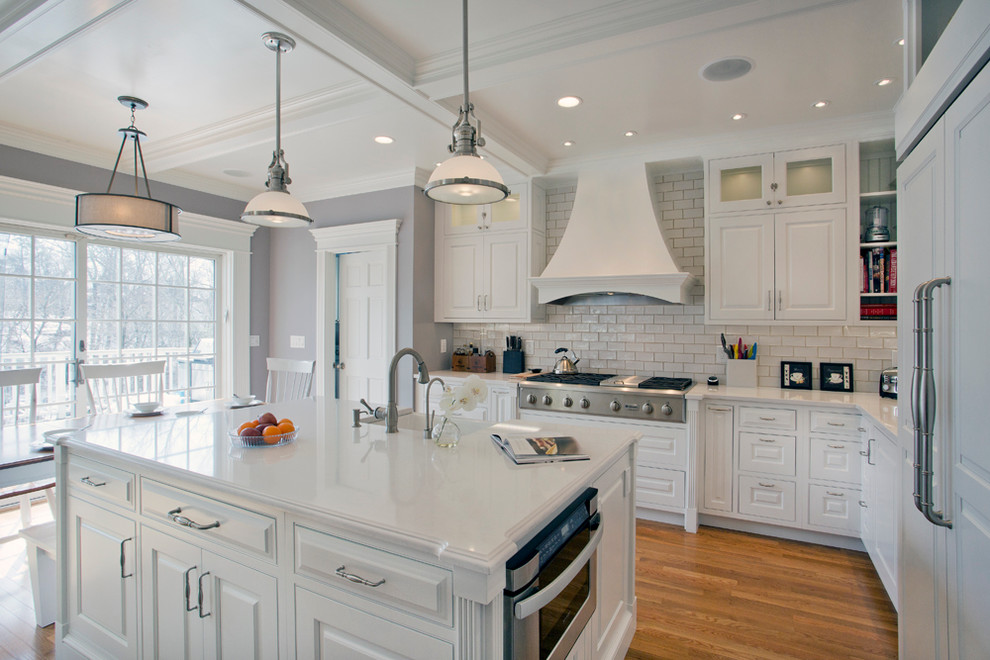 Inspiration for a large transitional l-shaped medium tone wood floor eat-in kitchen remodel with a farmhouse sink, white cabinets, granite countertops, white backsplash, stainless steel appliances, an island, raised-panel cabinets and subway tile backsplash