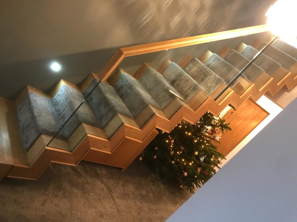 This is an example of a mid-sized modern wood straight staircase in Cheshire with wood risers and glass railing.