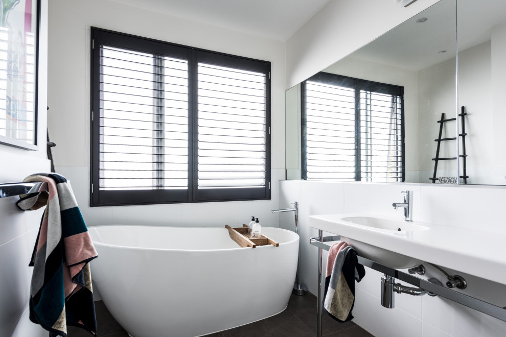 Photo of a contemporary bathroom in Melbourne with a freestanding tub, white tile, white walls, an integrated sink, black floor and white benchtops.