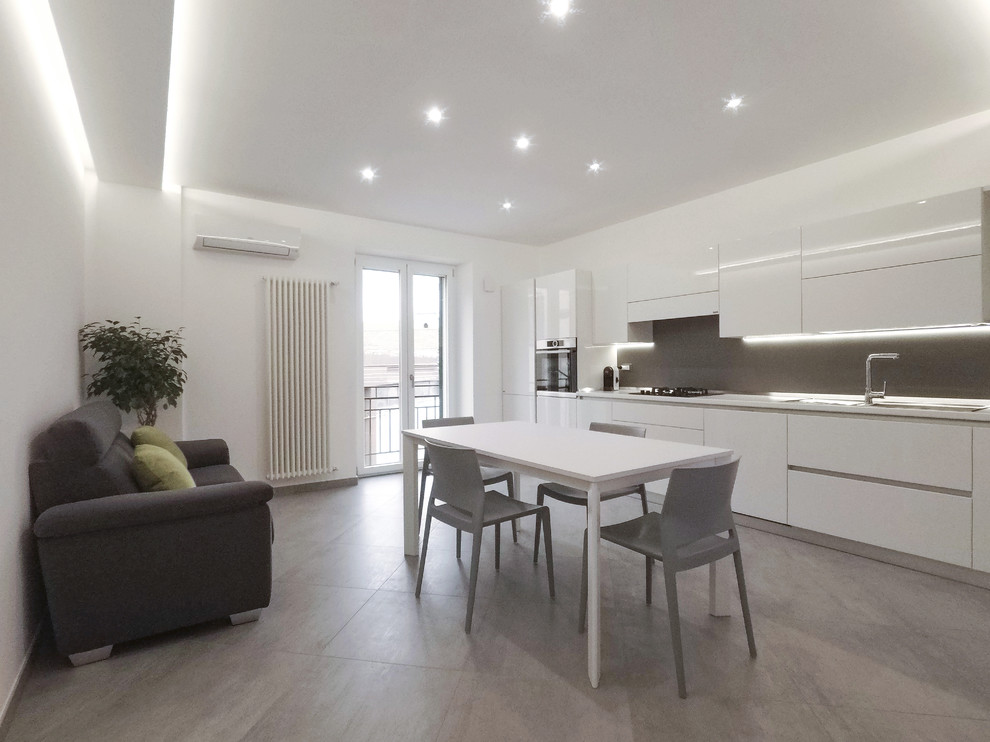 Design ideas for a mid-sized contemporary single-wall open plan kitchen in Bari with a drop-in sink, flat-panel cabinets, white cabinets, solid surface benchtops, grey splashback, porcelain splashback, stainless steel appliances, porcelain floors, no island, grey floor and white benchtop.