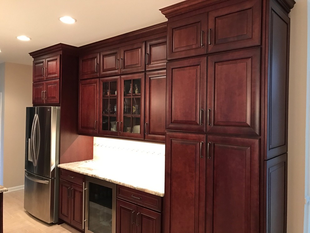 This is an example of a mid-sized mediterranean l-shaped eat-in kitchen in Newark with an undermount sink, raised-panel cabinets, dark wood cabinets, granite benchtops, beige splashback, stainless steel appliances, ceramic floors, with island, ceramic splashback, beige floor and beige benchtop.