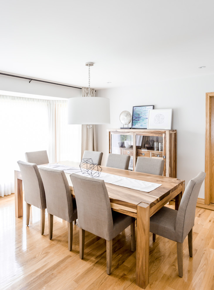 This is an example of a large beach style separate dining room in Montreal with white walls, light hardwood floors, no fireplace and brown floor.