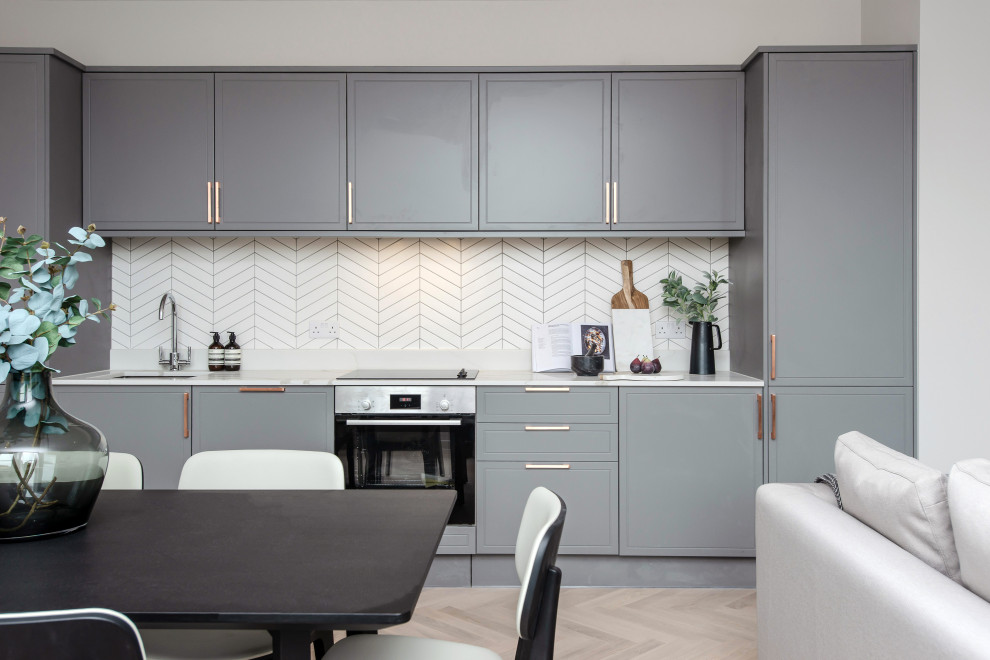 Inspiration for a small contemporary single-wall open plan kitchen in London with grey cabinets, quartzite benchtops, ceramic splashback, stainless steel appliances, light hardwood floors, no island, white benchtop, an undermount sink, flat-panel cabinets, white splashback and beige floor.