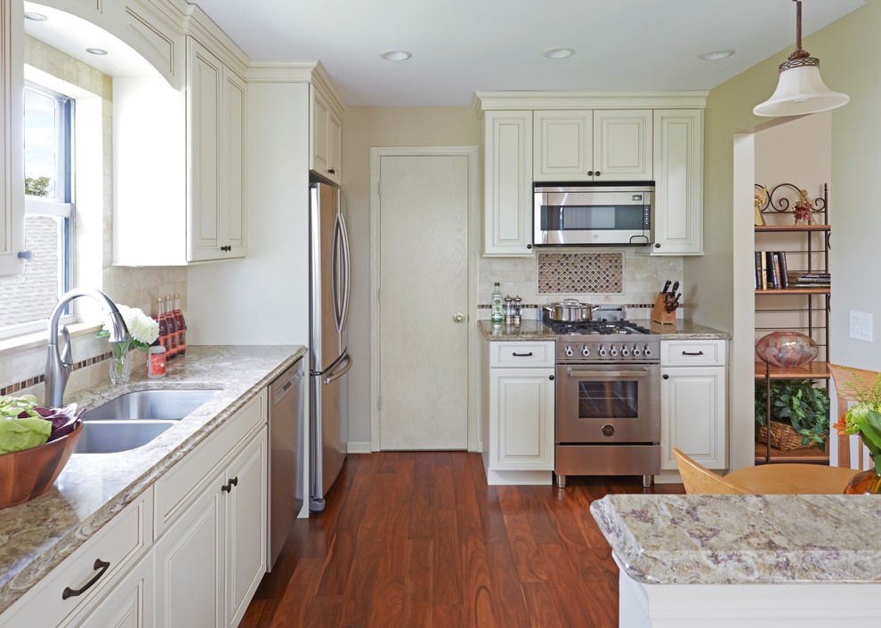 Example of a small classic l-shaped medium tone wood floor eat-in kitchen design in Chicago with a double-bowl sink, raised-panel cabinets, white cabinets, quartz countertops, beige backsplash, stone tile backsplash, stainless steel appliances and no island