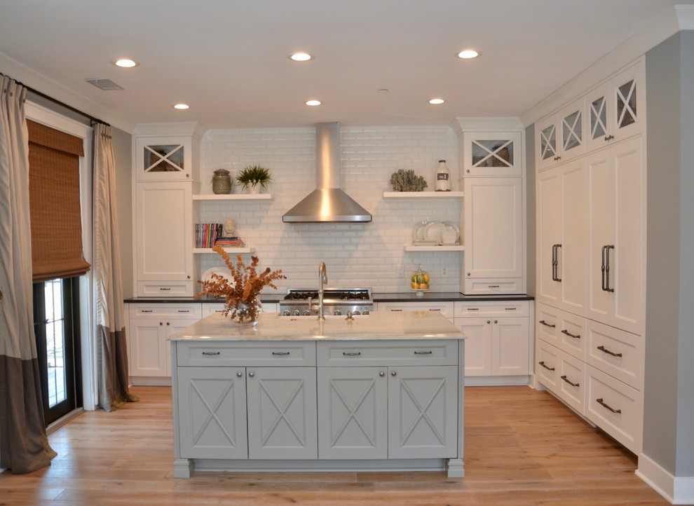 Example of a transitional light wood floor kitchen design in Atlanta with a farmhouse sink, flat-panel cabinets, white cabinets, quartzite countertops, ceramic backsplash and stainless steel appliances