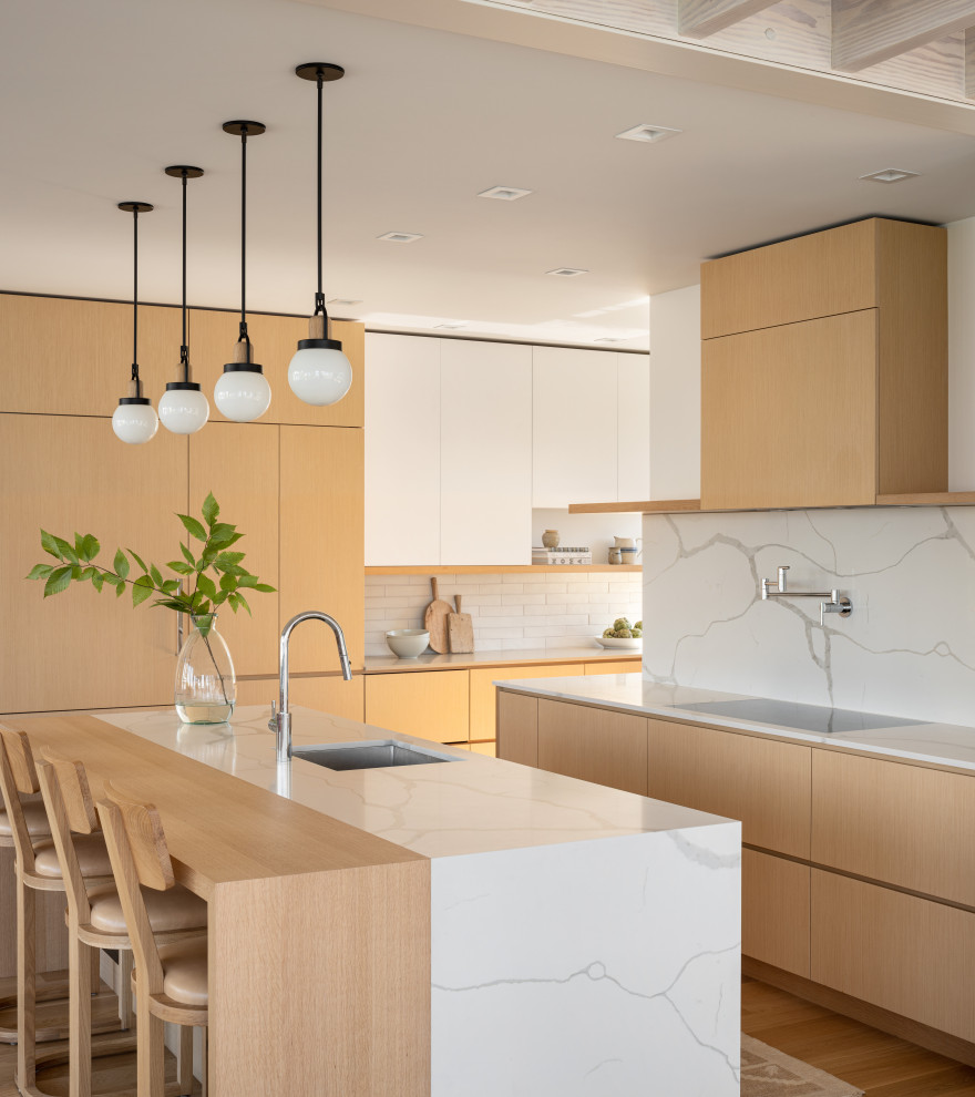 Inspiration for a beach style l-shaped kitchen in Portland Maine with an undermount sink, flat-panel cabinets, light wood cabinets, white splashback, stone slab splashback, medium hardwood floors, with island, brown floor and white benchtop.