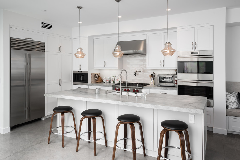 Open concept kitchen - mid-sized contemporary l-shaped concrete floor and gray floor open concept kitchen idea in Orange County with a farmhouse sink, shaker cabinets, white cabinets, white backsplash, stainless steel appliances, an island, marble countertops, subway tile backsplash and gray countertops