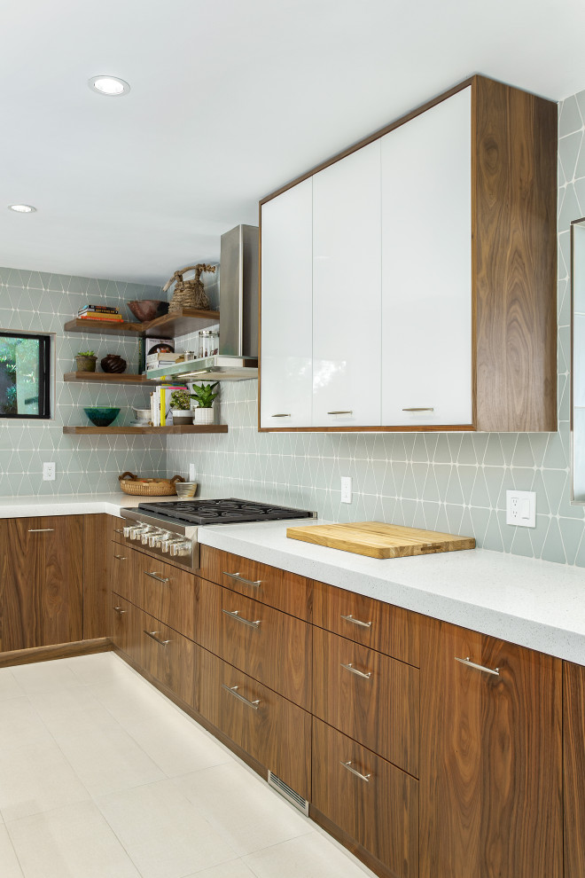 Inredning av ett modernt stort vit vitt kök, med en undermonterad diskho, släta luckor, skåp i mellenmörkt trä, bänkskiva i kvarts, blått stänkskydd, stänkskydd i glaskakel, rostfria vitvaror, klinkergolv i porslin, en halv köksö och svart golv