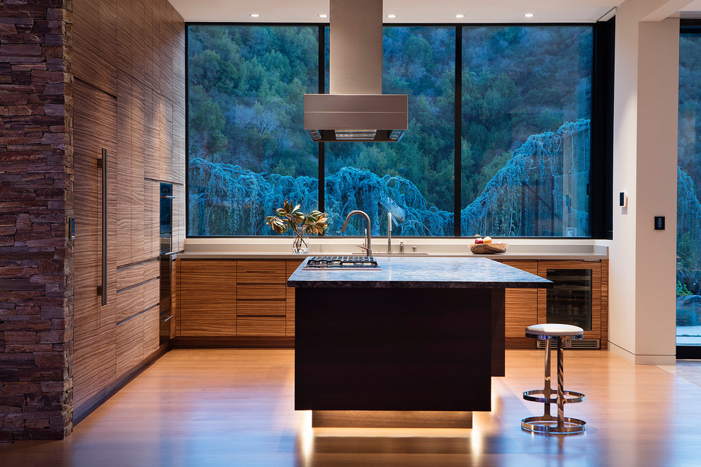 Inspiration for a mid-sized contemporary l-shaped open plan kitchen in San Francisco with a single-bowl sink, flat-panel cabinets, medium wood cabinets, quartz benchtops, grey splashback, stone slab splashback, panelled appliances, medium hardwood floors, with island, brown floor and grey benchtop.