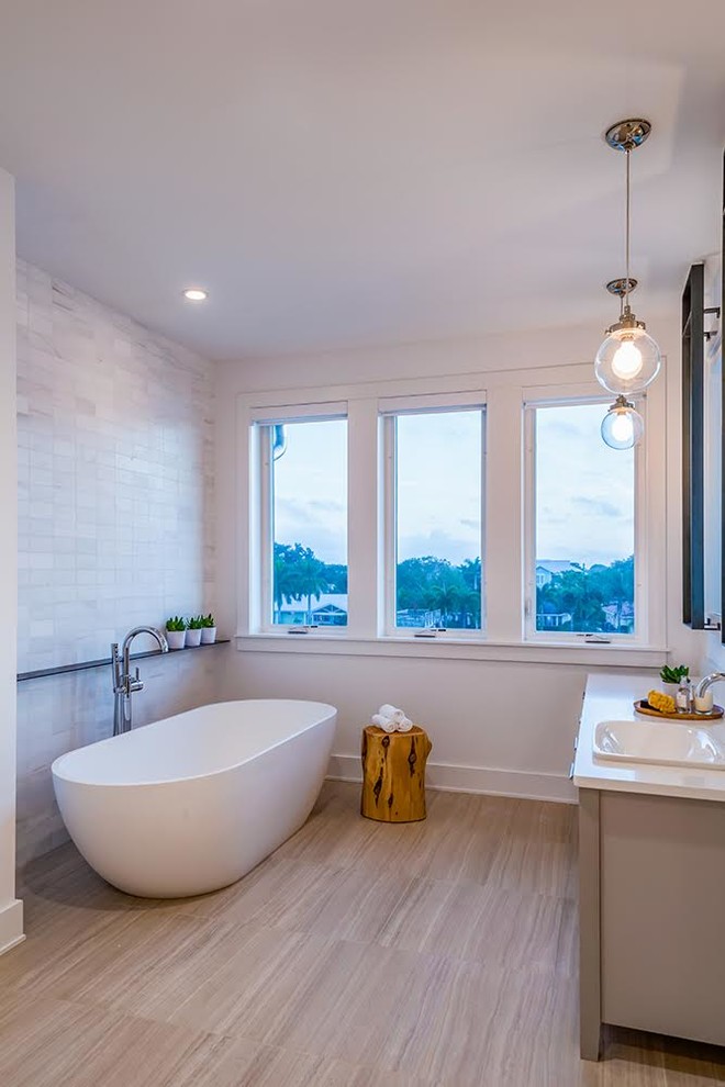 Photo of a mid-sized contemporary 3/4 bathroom in Tampa with beige cabinets, a freestanding tub, white tile, stone tile, white walls, light hardwood floors, a drop-in sink, solid surface benchtops, shaker cabinets and brown floor.