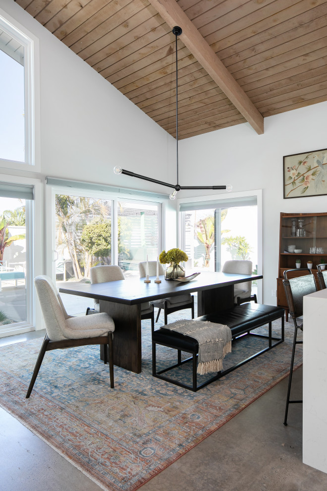 На фото: кухня-столовая среднего размера в стиле ретро с белыми стенами, бетонным полом, угловым камином, фасадом камина из кирпича, серым полом и балками на потолке с