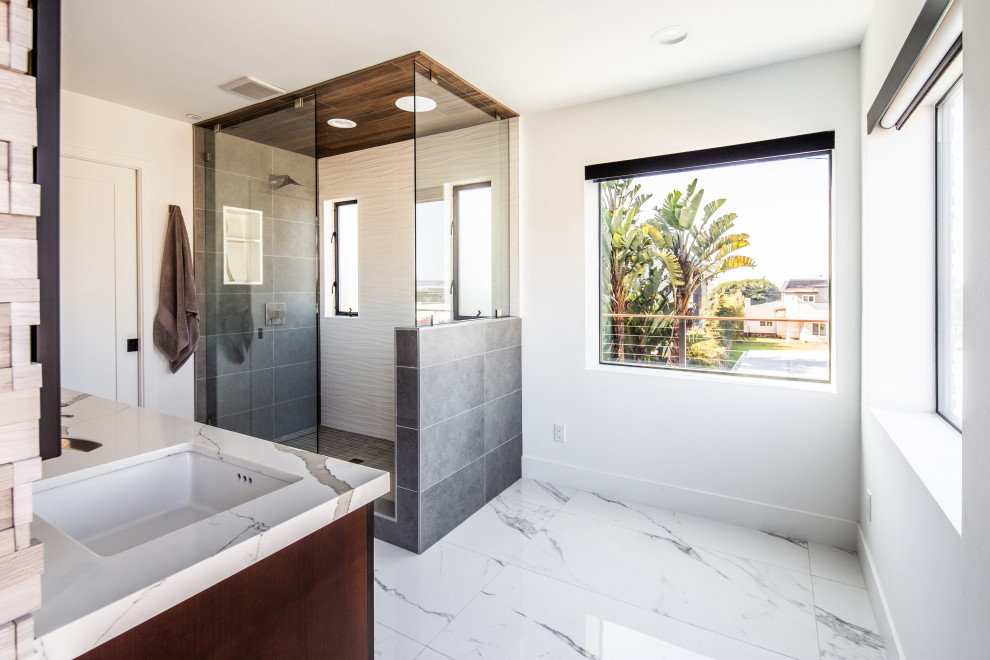 Inspiration for a large modern master bathroom in San Diego with flat-panel cabinets, brown cabinets, a double shower, gray tile, stone tile, white walls, porcelain floors, a drop-in sink, quartzite benchtops, white floor, a sliding shower screen, white benchtops, an enclosed toilet, a double vanity and a built-in vanity.