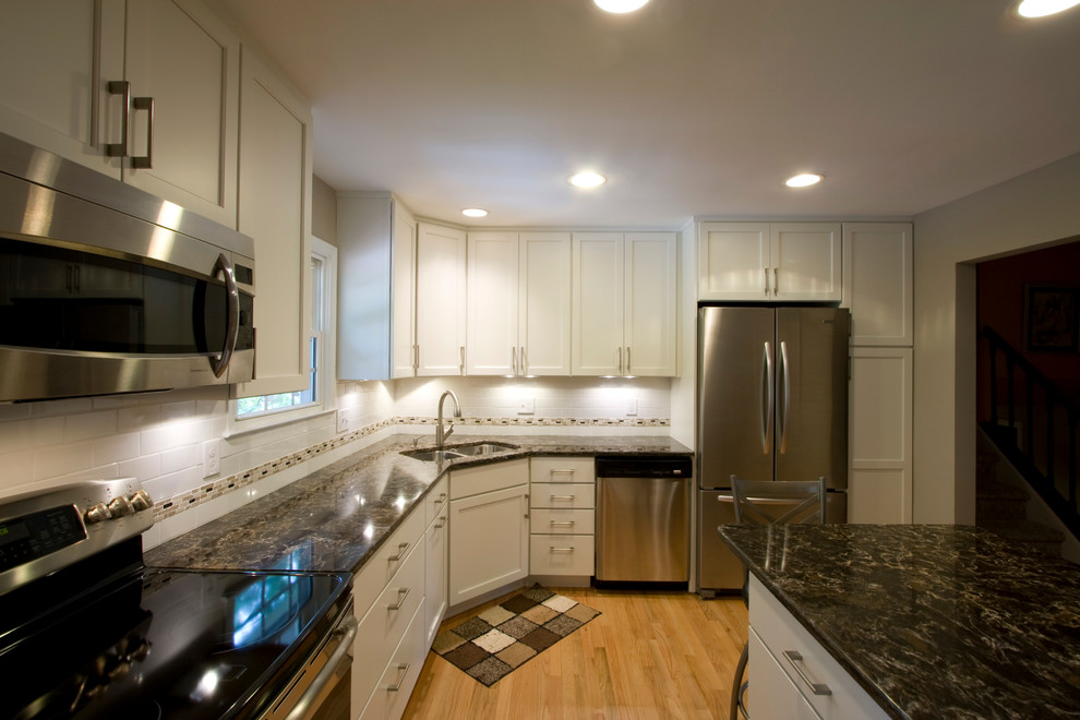 Enclosed kitchen - large transitional l-shaped light wood floor enclosed kitchen idea in DC Metro with an undermount sink, shaker cabinets, white cabinets, granite countertops, white backsplash, subway tile backsplash, stainless steel appliances and an island