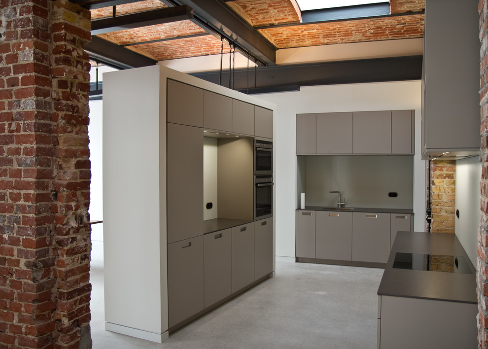 Inspiration for a mid-sized industrial separate kitchen in Berlin with flat-panel cabinets, grey cabinets, grey splashback, a single-bowl sink, panelled appliances and no island.