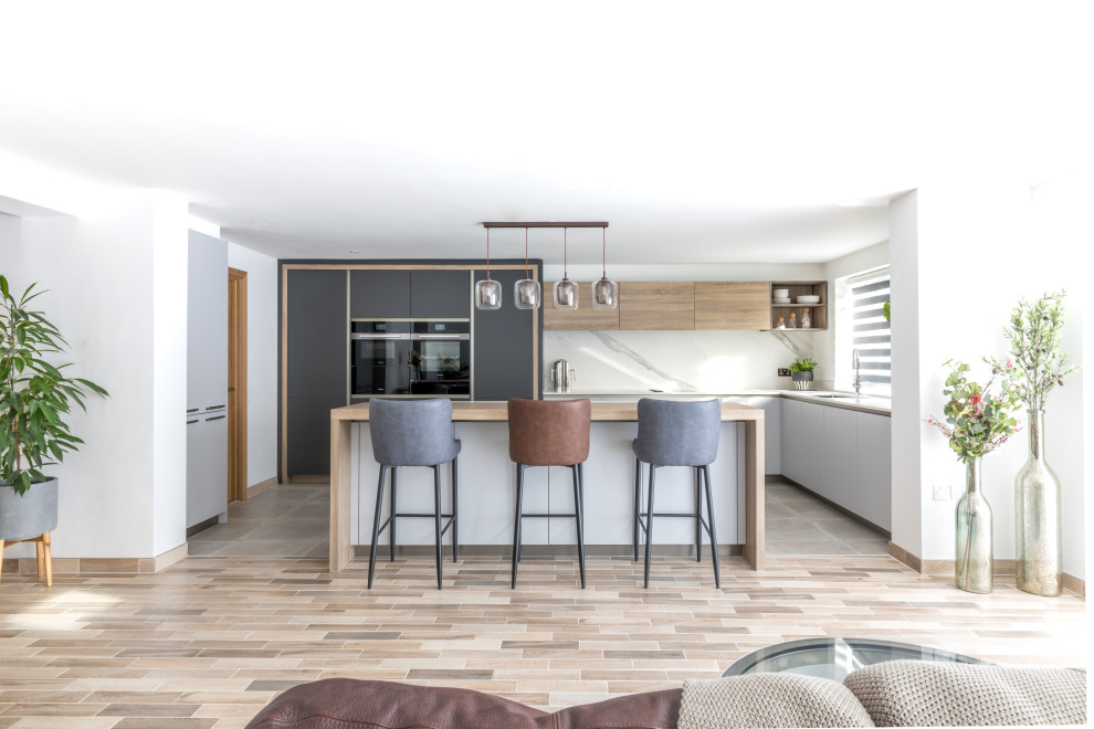 Design ideas for a medium sized contemporary l-shaped open plan kitchen in Sussex with flat-panel cabinets, grey cabinets, composite countertops, stainless steel appliances, an island and white worktops.