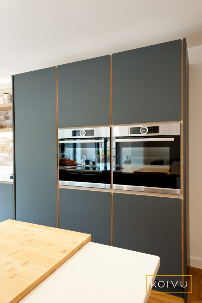 Inspiration for a mid-sized contemporary single-wall eat-in kitchen in Kent with a double-bowl sink, flat-panel cabinets, grey cabinets, solid surface benchtops, multi-coloured splashback, brick splashback, stainless steel appliances, medium hardwood floors, with island and white benchtop.