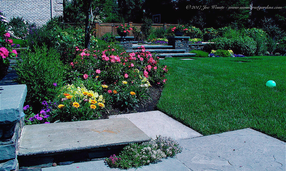 This is an example of a mid-sized traditional backyard partial sun formal garden in New York with a retaining wall and natural stone pavers.