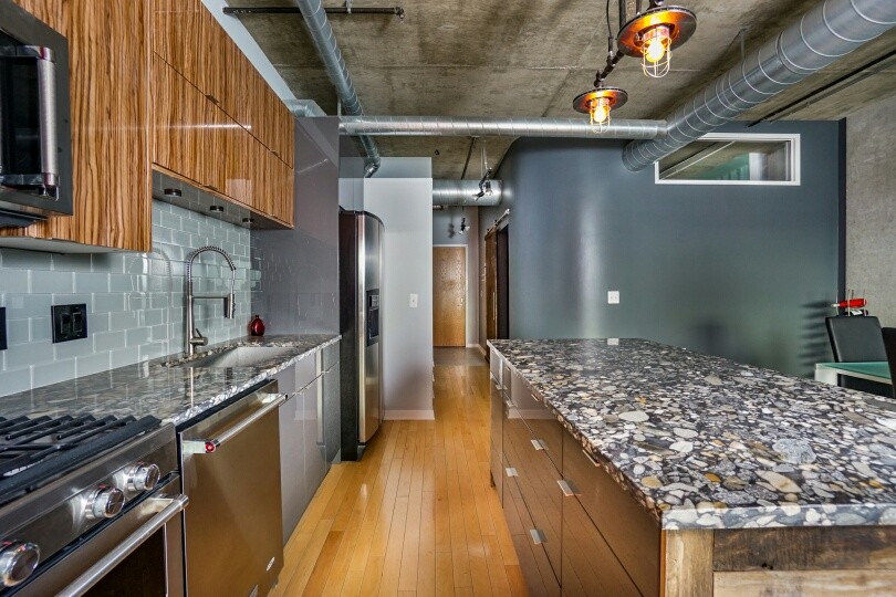 This is an example of a mid-sized industrial galley eat-in kitchen in Detroit with a single-bowl sink, flat-panel cabinets, medium wood cabinets, marble benchtops, grey splashback, glass tile splashback, stainless steel appliances, light hardwood floors and with island.
