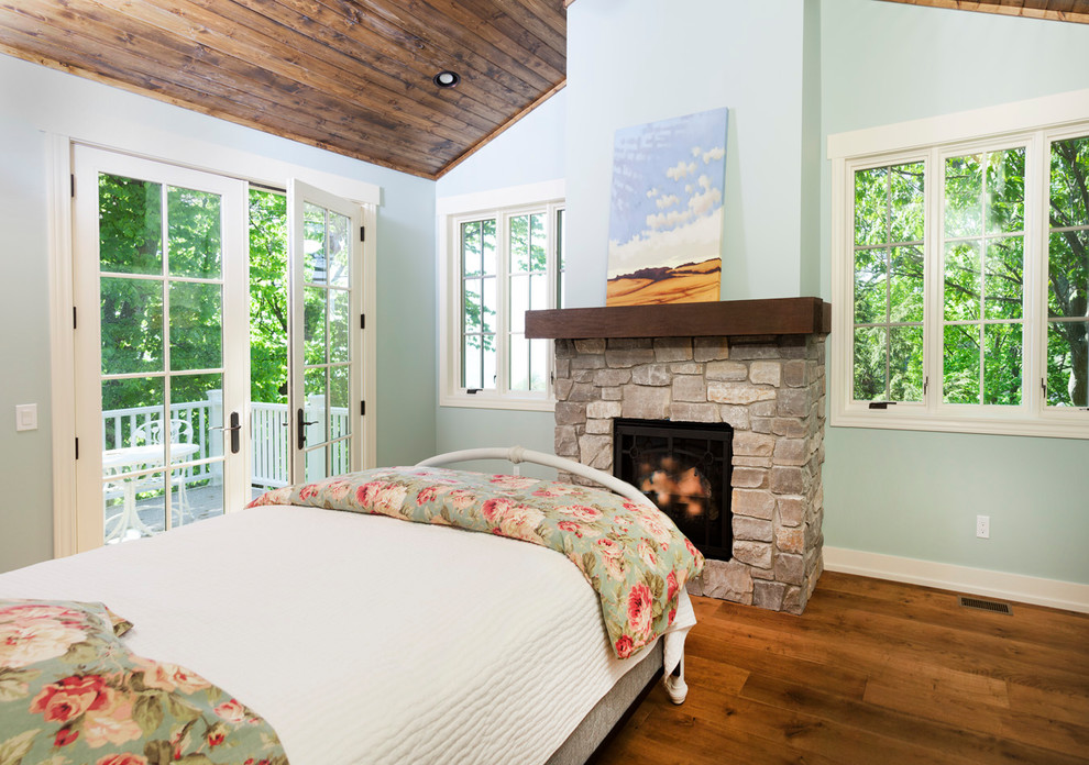 This is an example of a small beach style master bedroom in Grand Rapids with green walls, medium hardwood floors, a standard fireplace and a stone fireplace surround.