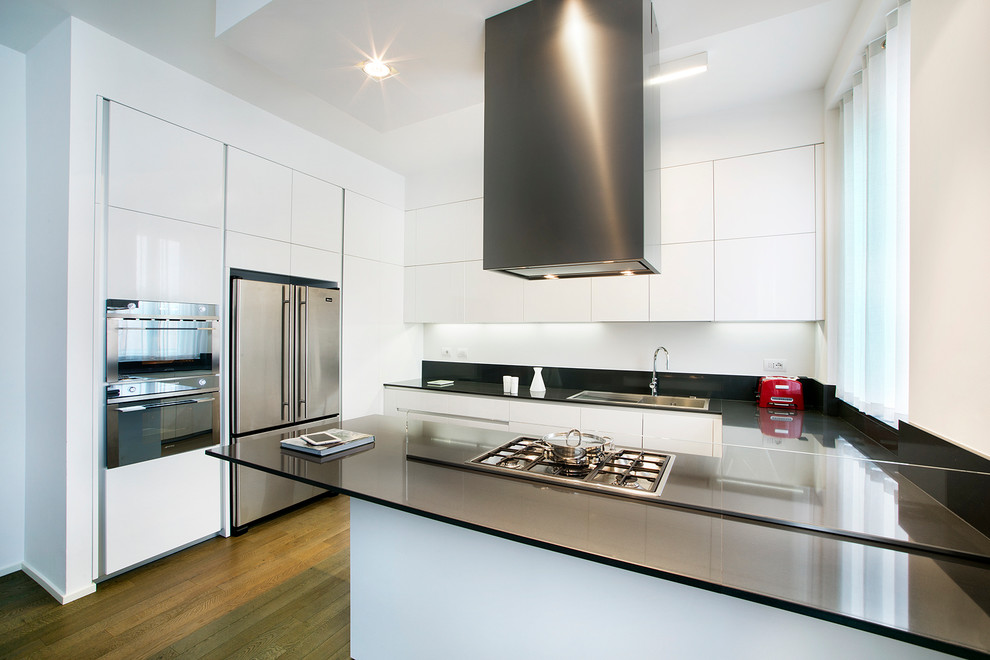 Photo of a contemporary u-shaped kitchen in Milan with a drop-in sink, white cabinets, stainless steel appliances, medium hardwood floors and a peninsula.