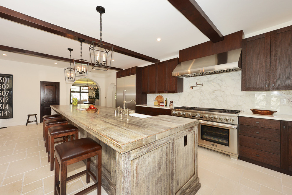 This is an example of an expansive mediterranean galley eat-in kitchen in Los Angeles with a farmhouse sink, recessed-panel cabinets, dark wood cabinets, white splashback, subway tile splashback, stainless steel appliances, travertine floors, with island and beige floor.