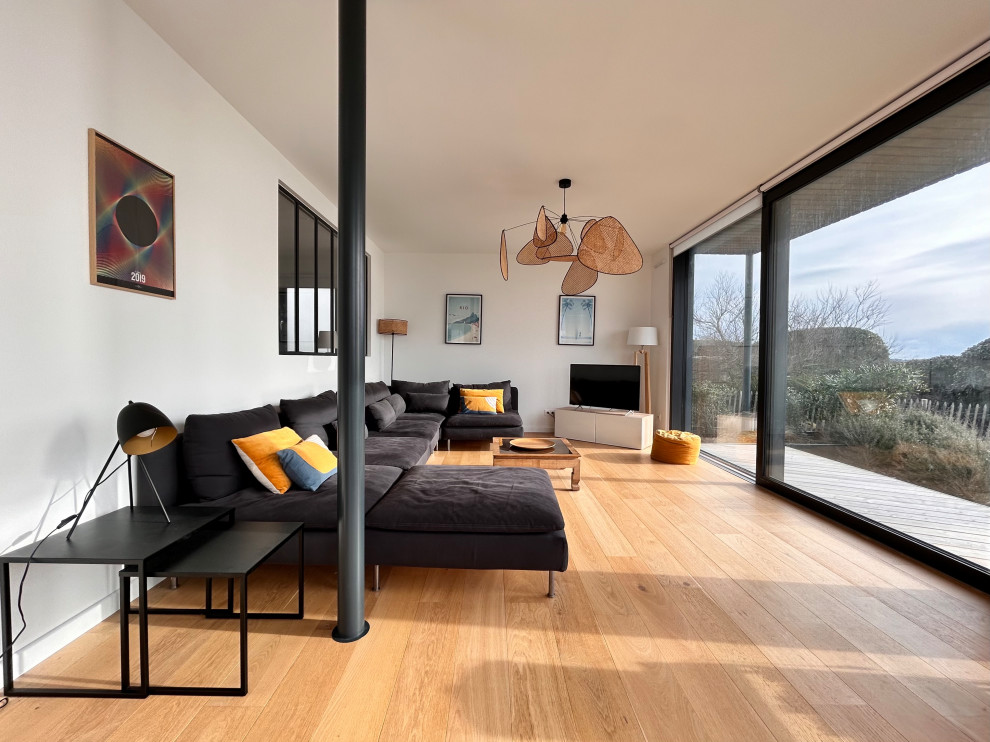 Imagen de salón abierto costero grande con paredes blancas, suelo de madera clara, televisor independiente y suelo beige