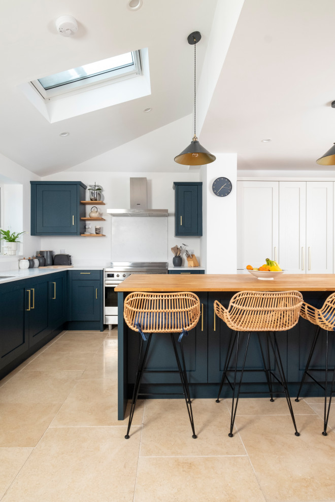 This is an example of a medium sized classic l-shaped open plan kitchen in Cardiff with shaker cabinets, blue cabinets, composite countertops, glass sheet splashback, stainless steel appliances, porcelain flooring, an island, beige floors, white worktops and a vaulted ceiling.