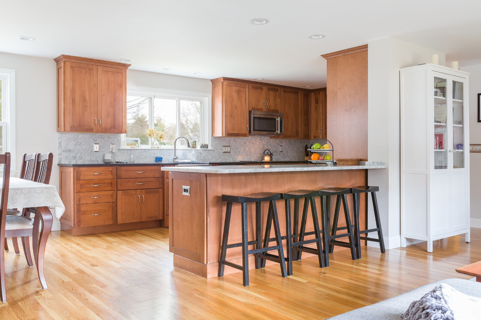 Example of a mid-sized transitional u-shaped medium tone wood floor eat-in kitchen design in Boston with a farmhouse sink, beaded inset cabinets, medium tone wood cabinets, marble countertops, gray backsplash, marble backsplash, stainless steel appliances, a peninsula and gray countertops