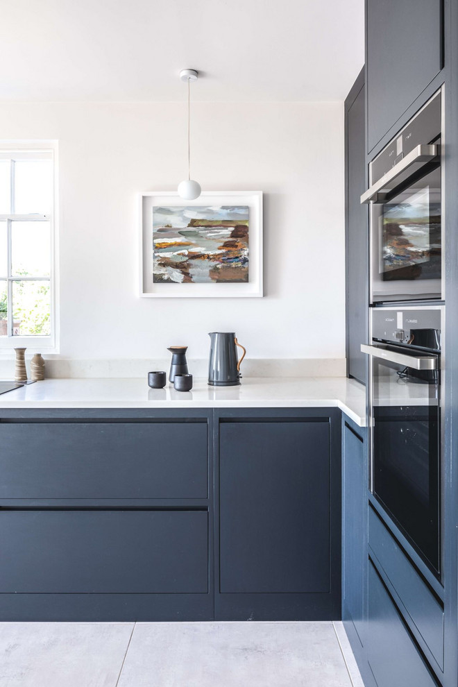 Design ideas for a mid-sized contemporary l-shaped eat-in kitchen in Gloucestershire with a drop-in sink, flat-panel cabinets, blue cabinets, quartzite benchtops, white splashback, black appliances, ceramic floors, no island, white floor and white benchtop.