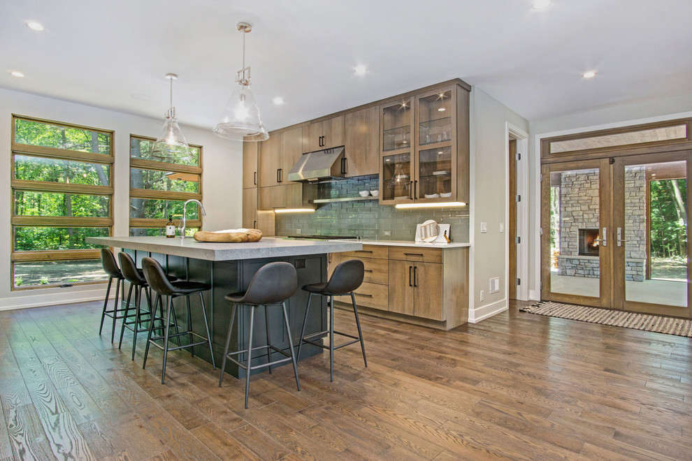 Inspiration for a rustic medium tone wood floor kitchen remodel in Grand Rapids with an undermount sink, flat-panel cabinets, quartz countertops, green backsplash, glass tile backsplash and stainless steel appliances