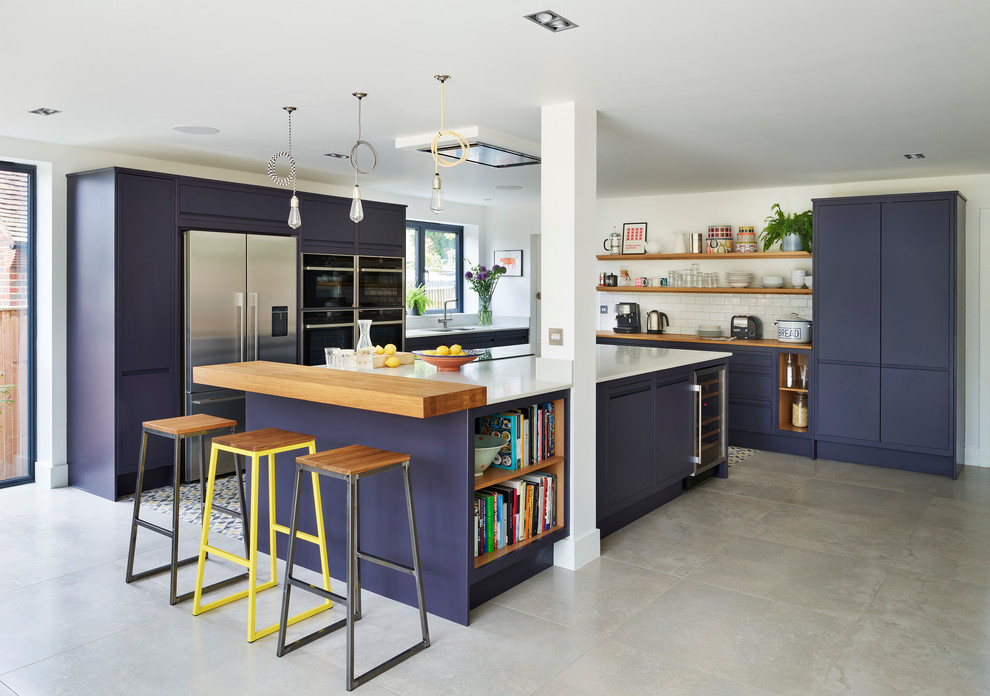 This is an example of a beach style l-shaped kitchen in Surrey with an undermount sink, flat-panel cabinets, blue cabinets, wood benchtops, white splashback, subway tile splashback, stainless steel appliances, with island and grey floor.