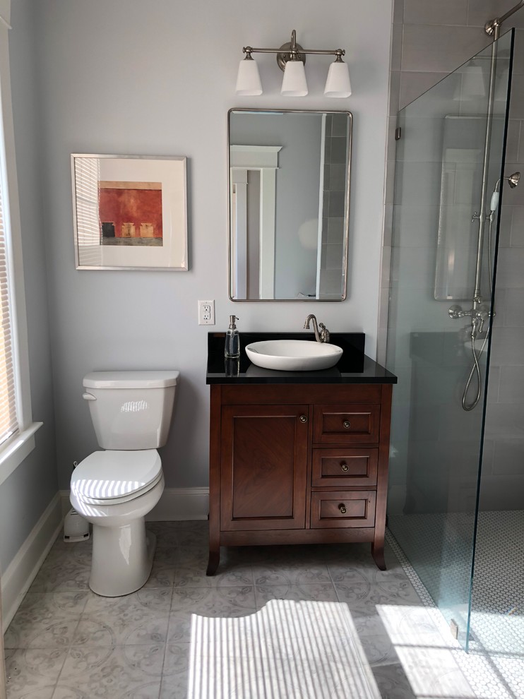 This is an example of a mid-sized transitional 3/4 bathroom in Baltimore with recessed-panel cabinets, dark wood cabinets, a curbless shower, a two-piece toilet, gray tile, ceramic tile, blue walls, ceramic floors, a vessel sink, granite benchtops, grey floor, an open shower and black benchtops.