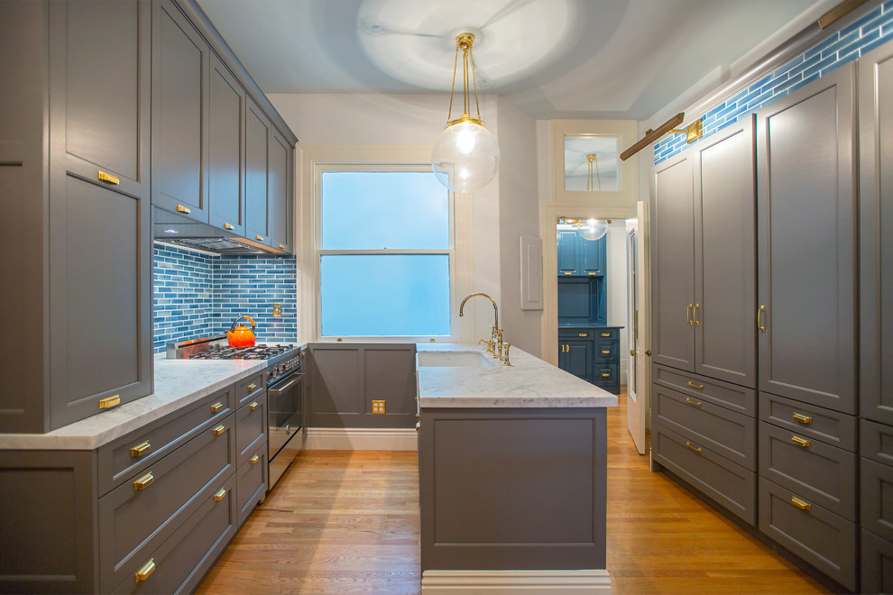 Photo of a traditional galley separate kitchen in San Francisco with a farmhouse sink, recessed-panel cabinets, grey cabinets, blue splashback, stainless steel appliances, medium hardwood floors and with island.