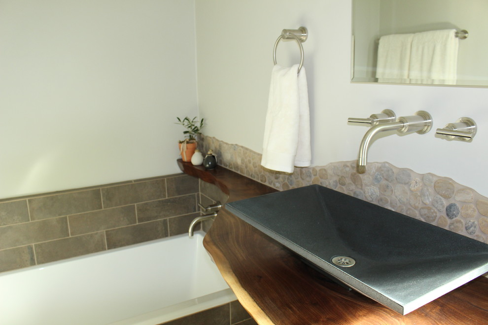 Photo of a small country bathroom in San Francisco with recessed-panel cabinets, grey cabinets, a drop-in tub, a corner shower, a one-piece toilet, brown tile, porcelain tile, grey walls, porcelain floors, a vessel sink and wood benchtops.