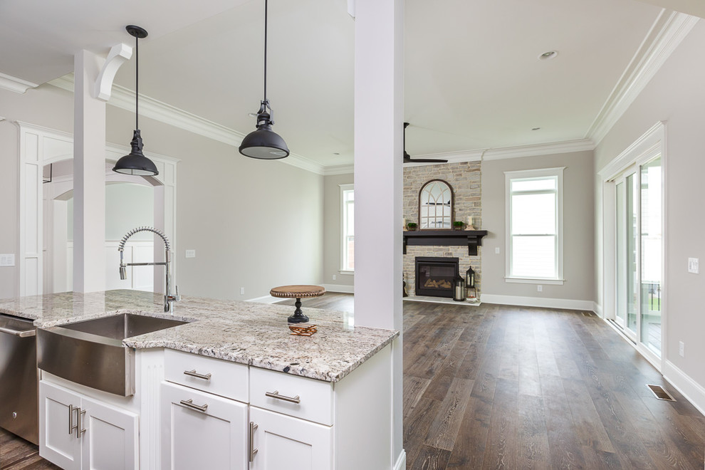 Inspiration for a mid-sized country single-wall open plan kitchen in Raleigh with a farmhouse sink, shaker cabinets, white cabinets, granite benchtops, white splashback, stainless steel appliances, dark hardwood floors, with island and brown floor.