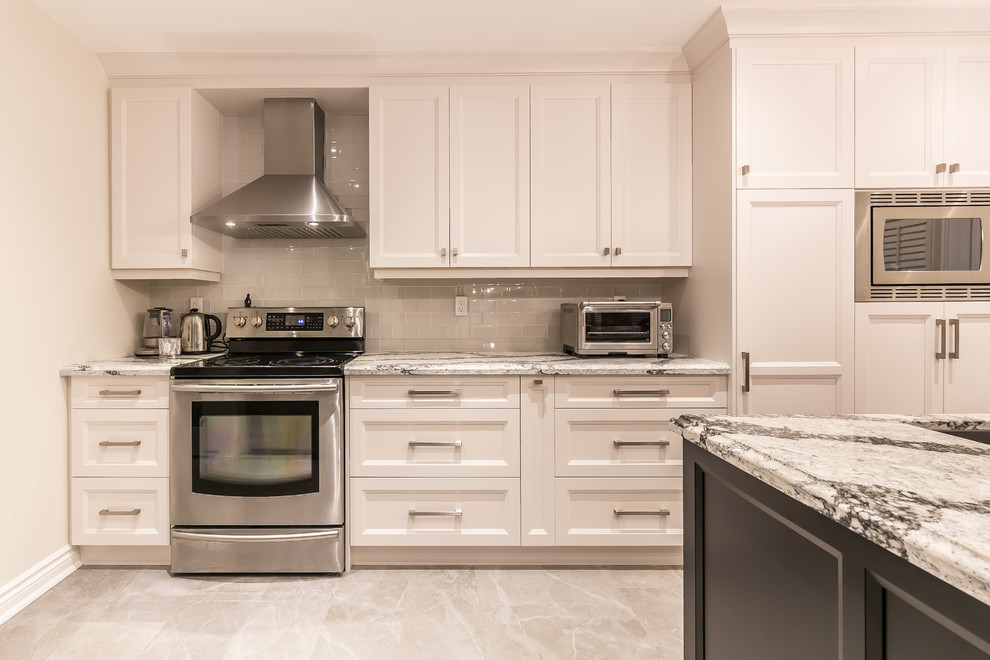 This is an example of a large transitional separate kitchen in Toronto with an undermount sink, recessed-panel cabinets, white cabinets, quartz benchtops, white splashback, ceramic splashback, stainless steel appliances, with island and grey floor.