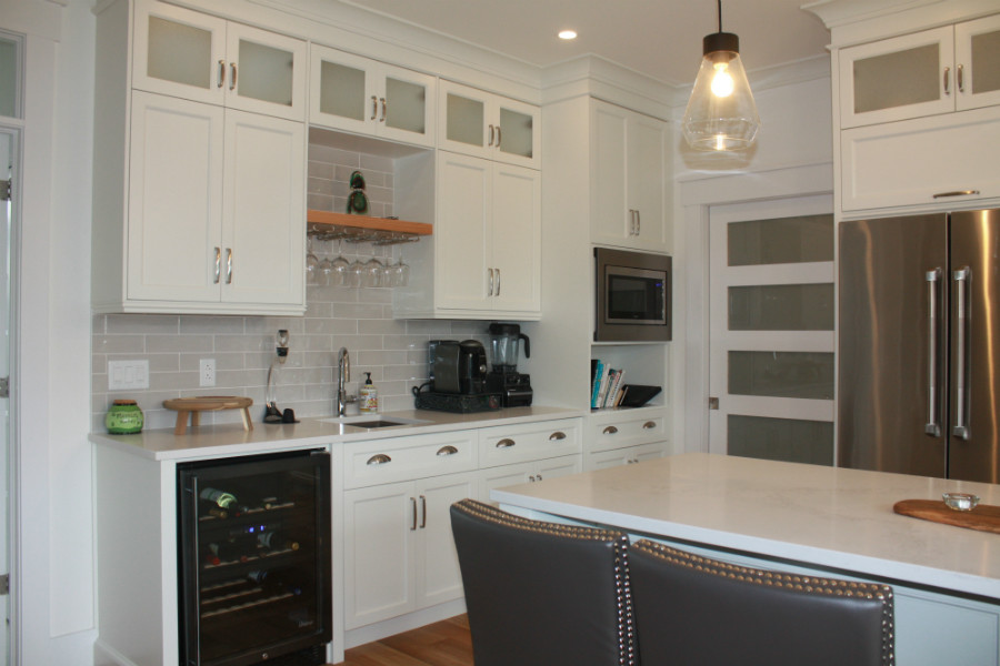 Example of a mid-sized transitional l-shaped medium tone wood floor kitchen pantry design with an undermount sink, shaker cabinets, white cabinets, quartz countertops, gray backsplash, cement tile backsplash, stainless steel appliances, an island and white countertops