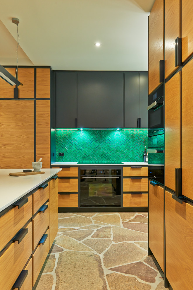 Design ideas for a mid-sized eclectic u-shaped eat-in kitchen in Adelaide with a double-bowl sink, beaded inset cabinets, medium wood cabinets, solid surface benchtops, green splashback, porcelain splashback, black appliances and with island.