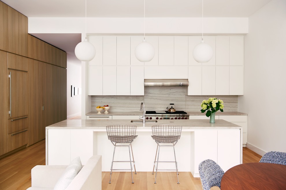 This is an example of a contemporary u-shaped eat-in kitchen in New York with an undermount sink, white cabinets, quartz benchtops, light hardwood floors, with island, brown floor, flat-panel cabinets, grey splashback, panelled appliances and grey benchtop.
