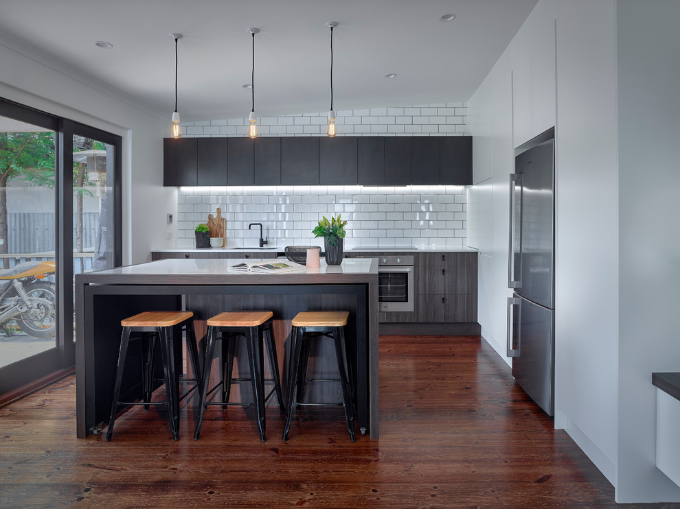 Inspiration for a large contemporary single-wall eat-in kitchen in Other with an undermount sink, white splashback, ceramic splashback, stainless steel appliances, medium hardwood floors, with island, flat-panel cabinets, dark wood cabinets, white benchtop and solid surface benchtops.