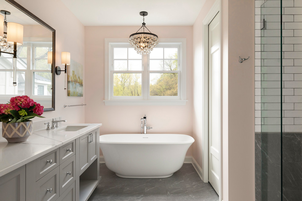 Photo of a beach style master bathroom in Minneapolis with shaker cabinets, grey cabinets, a freestanding tub, white tile, subway tile, pink walls, an undermount sink, grey floor and white benchtops.