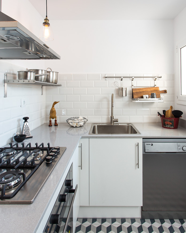 This is an example of a small industrial l-shaped separate kitchen in Barcelona with a drop-in sink, flat-panel cabinets, white cabinets, solid surface benchtops, white splashback, subway tile splashback, stainless steel appliances, ceramic floors and no island.