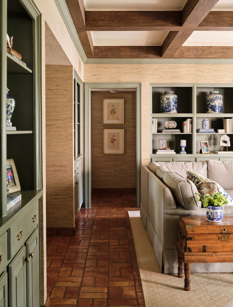 На фото: изолированная гостиная комната в классическом стиле с с книжными шкафами и полками, стандартным камином, балками на потолке, обоями на стенах, полом из терракотовой плитки, фасадом камина из кирпича и бежевыми стенами