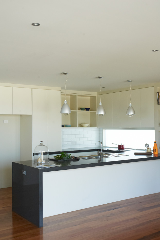 Photo of a large contemporary u-shaped eat-in kitchen in Melbourne with a double-bowl sink, flat-panel cabinets, white cabinets, granite benchtops, white splashback, ceramic splashback, stainless steel appliances, light hardwood floors and no island.