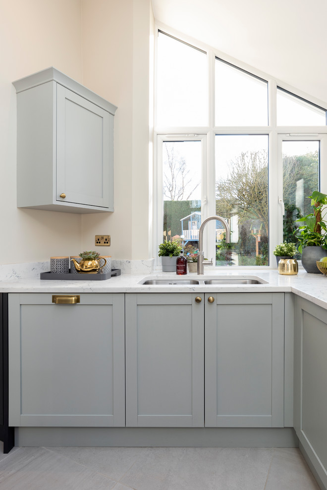 This is an example of a large contemporary galley eat-in kitchen in West Midlands with a drop-in sink, shaker cabinets, grey cabinets, marble benchtops, black appliances, ceramic floors, with island, white floor and white benchtop.