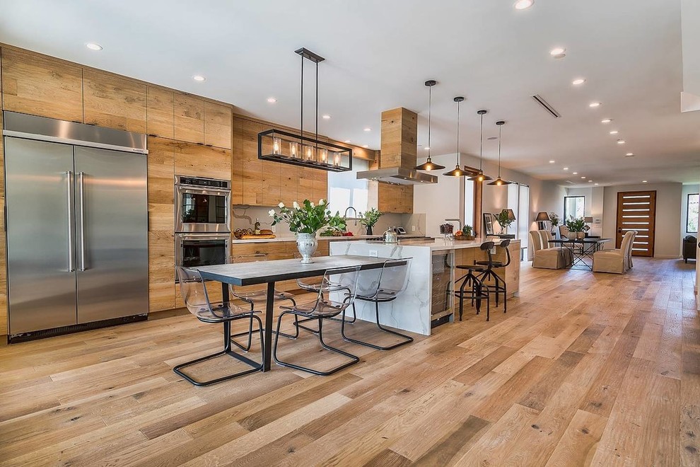 This is an example of a contemporary galley open plan kitchen in Los Angeles with flat-panel cabinets, medium wood cabinets, white splashback, stainless steel appliances, medium hardwood floors, with island and brown floor.